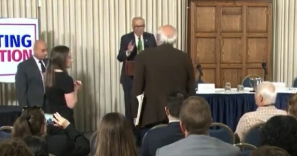 WATCH: “Please Sit Down!” – Schumer’s Anti Trump Speech Interrupted by Liberal Heckler Screaming, “How Dare You Talk About Corruption… Genocidal Maniac. Shame!”